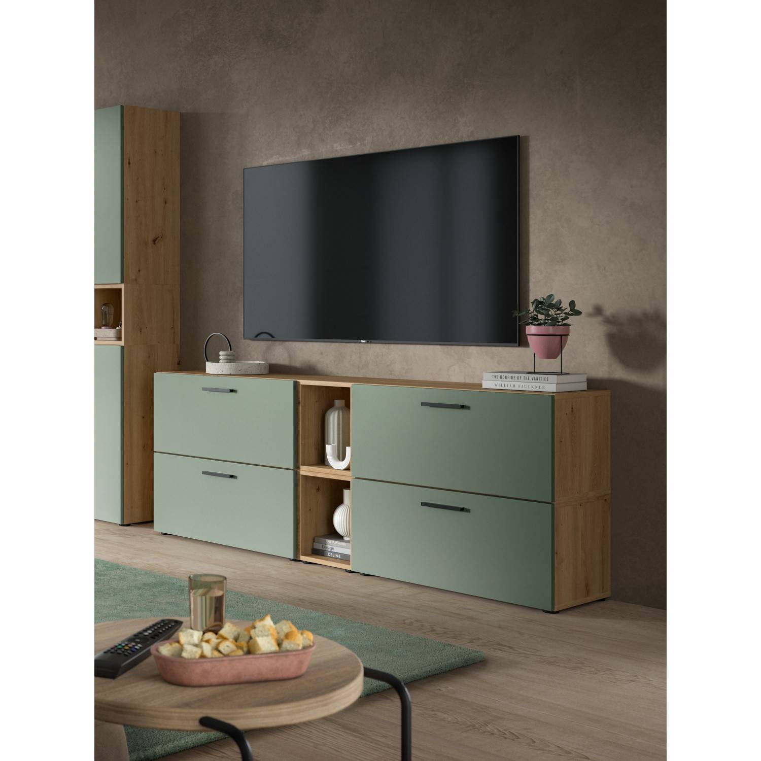 Kompakte Wohnwand mit grünen Fronten und Holzoptik unter einem Fernseher im Wohnzimmer – Jonni